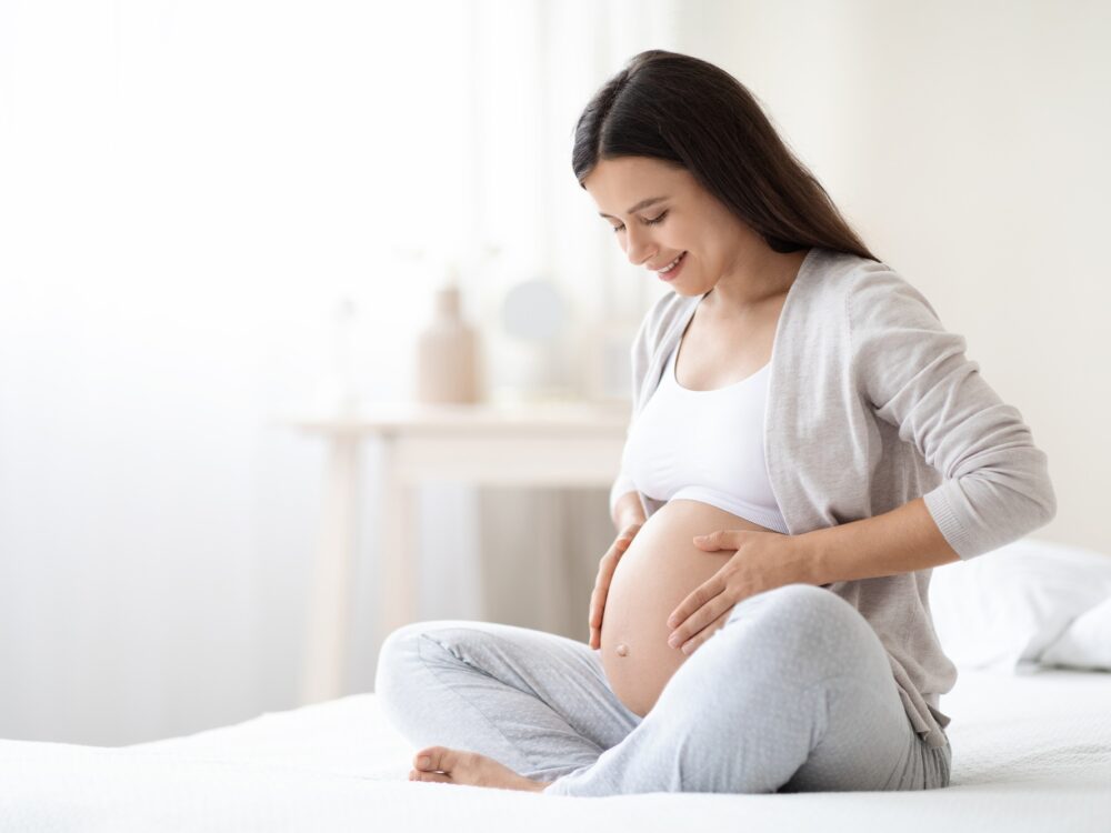 Smiling pregnant woman sitting on bed in her bedroom